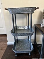 Side view of the three-tier galvanized metal floor storage unit with wooden handles on the top tier.