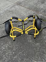 Yellow kayak carrier cart with black foam padded bars and large airless tires shown folded and lying on asphalt.