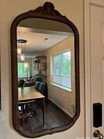 Full view of the vintage mirror hanging on the wall showing the carved wood frame and reflection of the dining area.