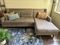 Front view of brown fabric West Elm sectional sofa with chaise, sitting on patterned area rug with four decorative throw pillows.