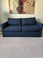 Front view of regal blue West Elm Harris queen sleeper sofa with two seat and two back cushions, against light neutral wall and carpet.