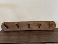 Front view of the wooden wall rack showing 5 brass-tipped pegs spaced evenly on the acorn finish wooden base.