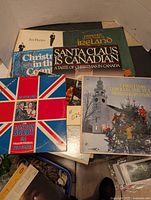 Top view of several Christmas and traditional music vinyl albums stacked, showing titles including Jan Peerce, Santa Claus is Canadian, Passport to Ireland.