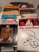 Photo showing collection of 12 vintage vinyl records with various artists and titles visible.