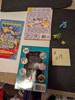 Three Pokémon books arranged side by side with colorful covers. Three mini figurines placed nearby on a surface; blue Dratini, green Bayleef, and yellow Pikachu.