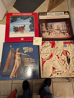 Four vinyl record albums arranged on floor showing covers: Country Christmas with snowy horse and sleigh scene, H.M.S. Pinafore theatrical stage photo, Thais with female figure in costume, Offenbach La Périchole illustrated cover with dancing figures.