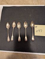 Full top-down photo showing all five silver spoons laid out side by side on a dark surface.