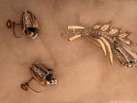 Photo showing one brooch and the two matching clip-on earrings placed on a beige surface, highlighting the rhinestones and design details.
