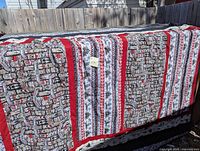 Quilt side with totem poles pattern in brown, red, and white colors hanging outdoors on a wooden fence