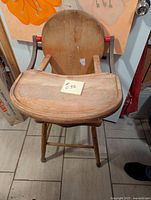 Front view of children's high chair showing the rounded hardwood backrest, fold-over tray with some surface wear, and four legs.