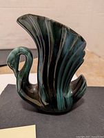 Single blue-green swan-shaped vase showing profile with detailed wings forming the vase opening, highlighted dark strokes in glaze.