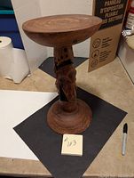 Full view of carved wooden plant stand showing round top, carved figure support, and round base.