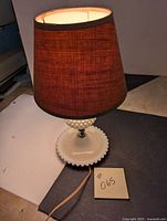 Front-side view of the small milk glass table lamp with brownish fabric shade, showing the lamp and electrical cord with plug.
