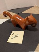 Front side view of the carved wooden squirrel figurine, showing the nut in its mouth and smooth finish.