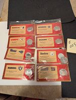 Eight sealed Budweiser Super Bowl commemorative coins with cards for Redskins, Cowboys, Chiefs, Bears, Rams, Steelers, Raiders, and Giants.