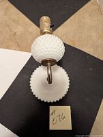 Top-down view of wall light showing milk glass hobnail globe and scalloped base along with metal socket and arm