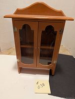 Front view of wooden cabinet showing top curved edge, two glass paneled doors, and small round knobs.