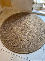 Photo of round area rug with beige and burgundy floral patterns laid on tiled floor near doorway.