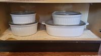 Four white ceramic casserole dishes with ribbed sides in various sizes, some with clear glass lids.