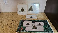 Photo of seven plastic Christmas trays of varying sizes, all with white base featuring Christmas tree design in the center, set on granite countertop.