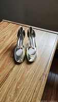 Front view of gold high heel shoes on wooden surface, showing peep-toe style