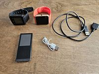 Samsung YP-T10 media player, two smart watches, and two charging cables arranged on wooden table.