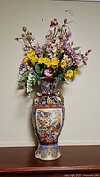 Full view of the tall ornate ceramic vase with artificial flowers, showcasing detailed floral and bird motifs and multi-colored flower arrangement.