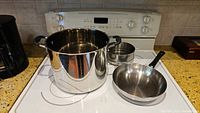 Full view of large stainless steel pot, steamer insert, and frying pan on stove top
