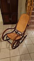 Full view of rattan rocking chair showing woven seat and backrest with curved wooden armrests and rockers