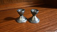 Pair of small sterling silver weighted candle stick holders placed on wooden surface, showing overall shape and oxidized patina.