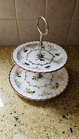 Photo of two-tier ceramic tea cake stand with floral pattern and gold trim and metal handle