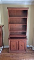 Front view of the tall wooden bookcase with shelves and cabinet below.