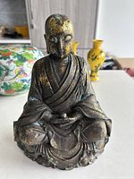 Front view of the antique bronze Buddhist statue showing detailed robes, serene facial features, seated cross-legged with bowl in hands.