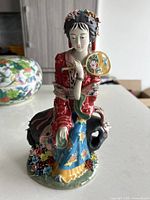 Front view of the figurine showing the woman’s face, attire, and hand fan