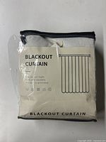 Front view of the blackout curtain in sealed plastic packaging showing the label with product type, fabric description, and care instructions.