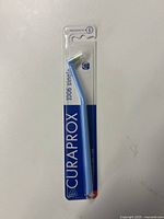 Front view of the Curaprox 1006 toothbrush in original packaging showing the blue angled slim toothbrush visible inside clear plastic blister pack, with brand and model name on cardboard backing.
