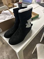 Side and front view of black slouch ankle boots with bow detail, padded interior visible.