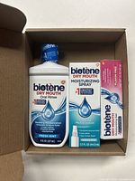 Top-down view of the Biotene dry mouth oral care products inside an open cardboard box showing the mouth rinse, moisturizing spray, and toothpaste in sealed packaging.