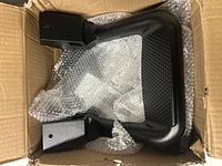 Pair of black aluminum side steps in a box with bubble wrap, showing curved step with square mounting tubes.
