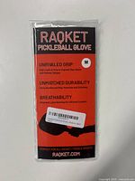 Front view of the packaged Raqket Pickleball Glove with branding and product details visible, highlighting size Medium and black color.