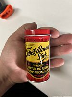 Front view of Tibet Almond Stick metal tin showing product name and usage info for furniture and flooring scratch removal.