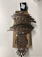 Top view of wooden owl wall decor showing detailed carved wood design and solar panel on top, placed on a cardboard box.