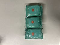 Three sealed teal packs of deodorant wipes arranged vertically on a white surface.