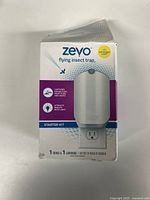 Front view of Zevo flying insect trap box showing product branding, key features like capture and attract properties, and starter kit contents.