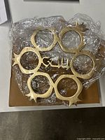 Chandelier parts wrapped in plastic showing gold metal pieces shaped like pomegranates with star tops.