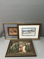 Three framed art lithographs arranged with one flat on surface and two against wall. Varied artistic subjects and wooden frames