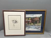 Photo of two framed signed lithographs: portrait of young girl and old mill buildings by a river.