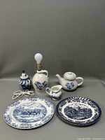 Full view of ceramic and pottery items including lamp, teapot, creamer, jar, and decorative platters, all featuring blue floral or scenic patterns on a white background.