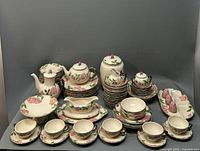 Front view displaying the full set including cups and saucers, teapots, serving bowls, gravy boat, comport dish, and various plates.