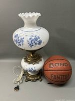 Full view of the floral lamp with electric cord and plug, showing floral pattern, brass fittings, and ruffled white glass top.